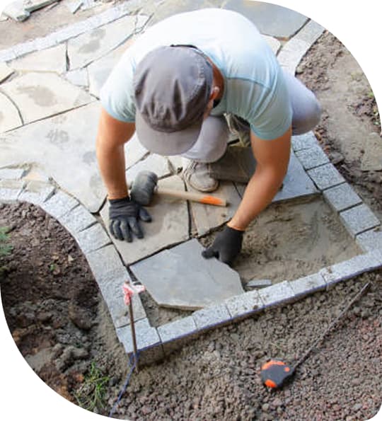 Mann verlegt Steinplatten um einen Gartenweg zu fliesen